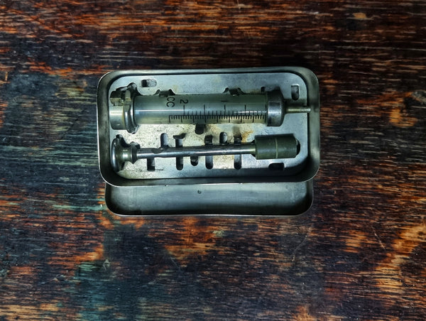 Vintage glass hypodermic syringe in metal tin